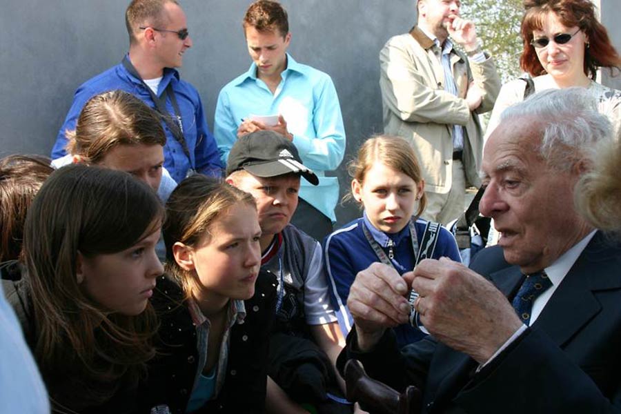 Yosef Bienenstock speaking with students in Germany, and Yuval in the background.