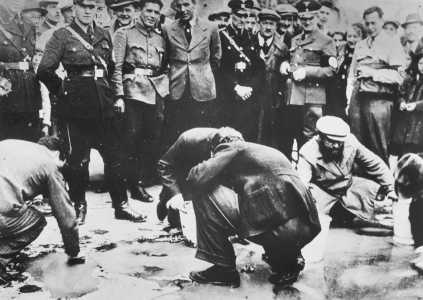 Austrian Nazis and local residents look on as Jews are forced to get on their hands and knees and scrub the pavement in Vienna. Date: March 1938 - April 1938.